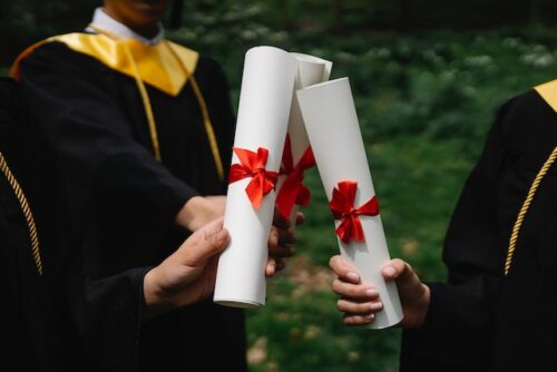 two graduates holding diplomas
